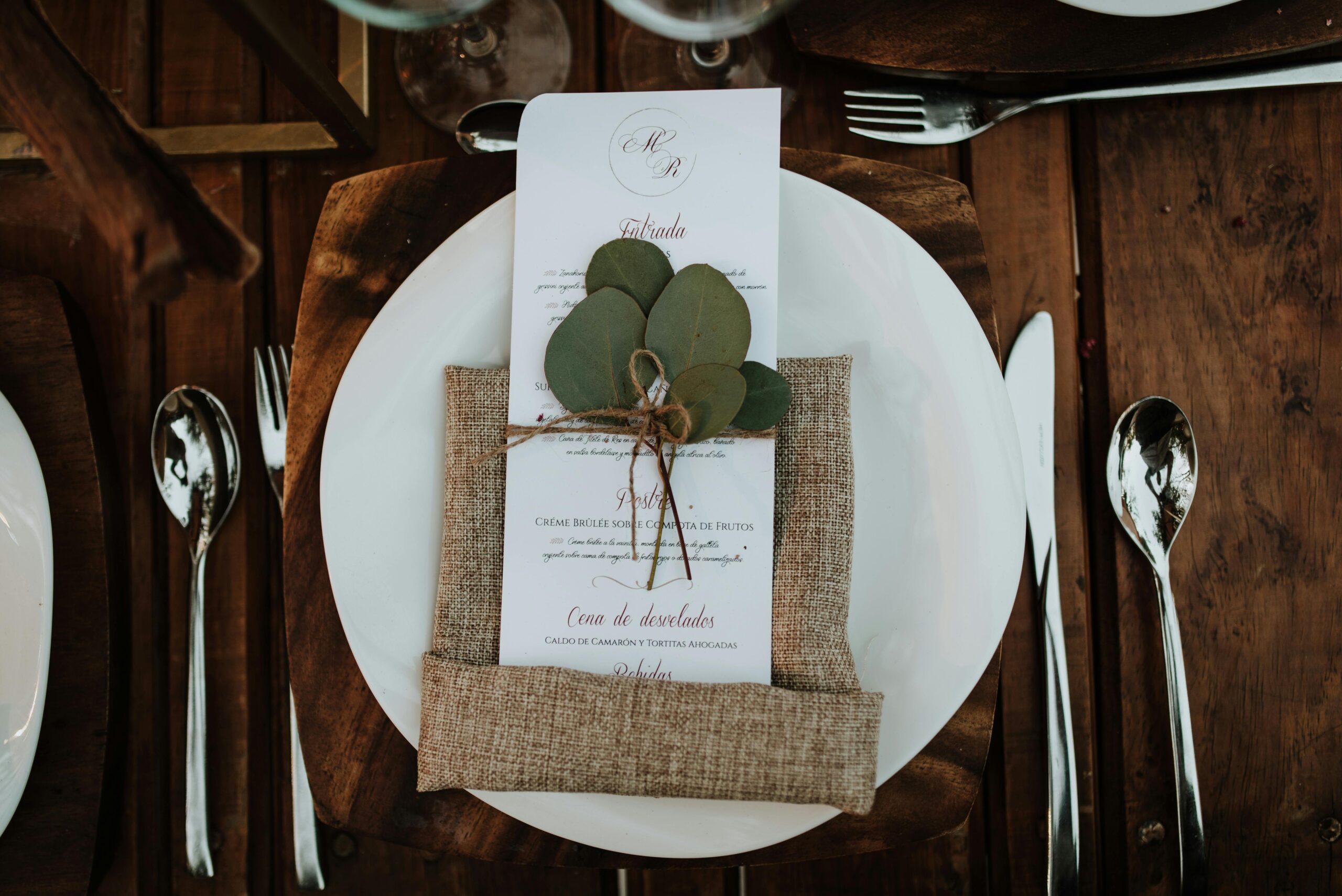 Stylish table setup featuring a menu card with eucalyptus leaves on a rustic wooden table.